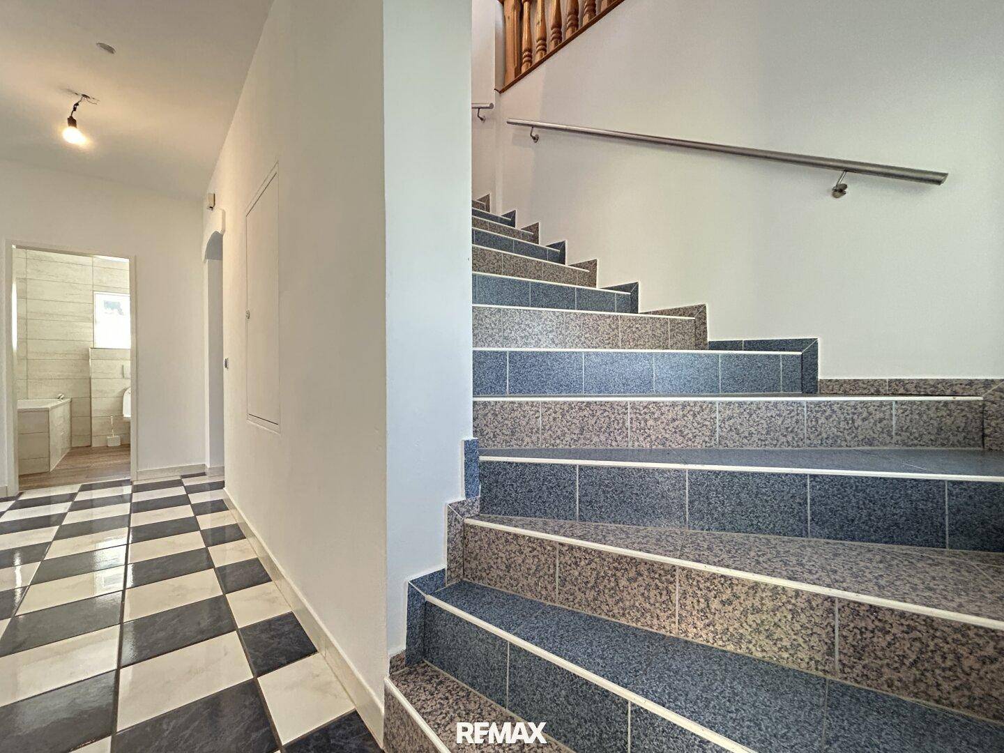 Heller Flur mit gefliestem Schachbrettmusterboden und Treppe ins Obergeschoss.