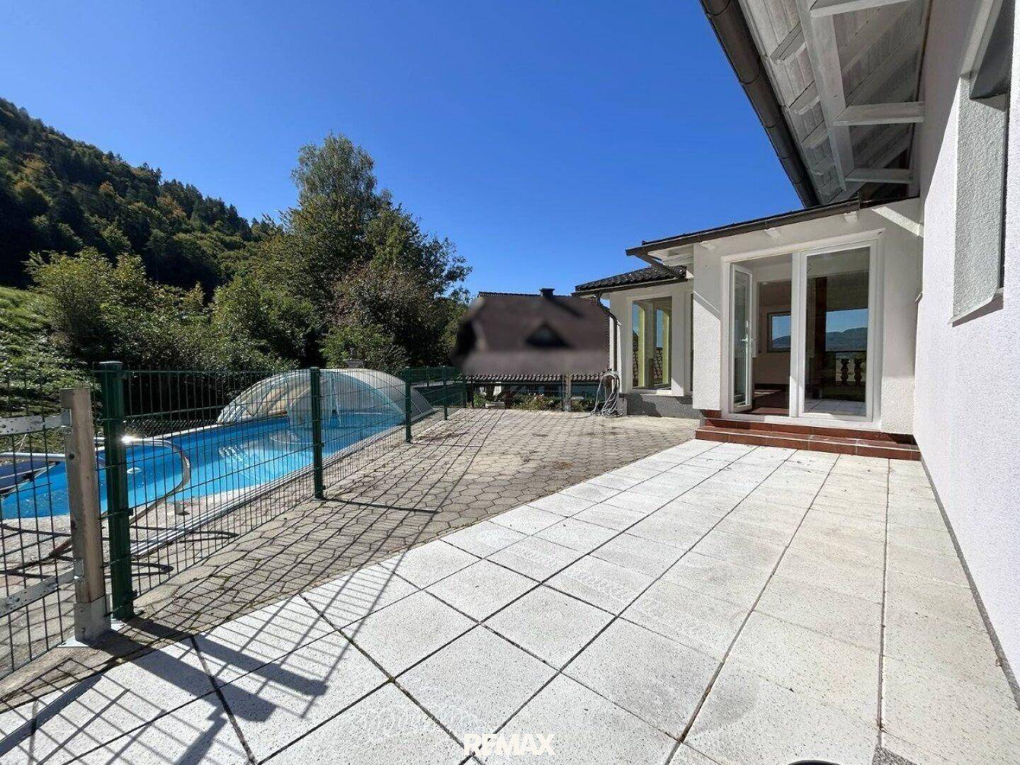 Große gepflasterte Terrasse mit Zugang zum Pool und Blick auf die bewaldeten Hügel.