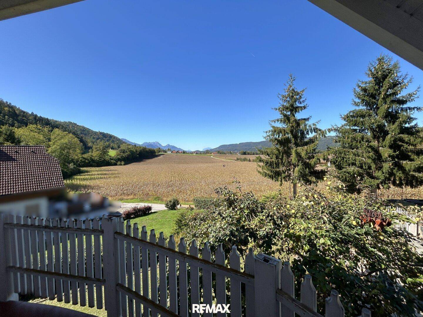 Panoramablick vom Balkon auf weite Felder, grüne Hügel und ferne Berge unter blauem Himmel.