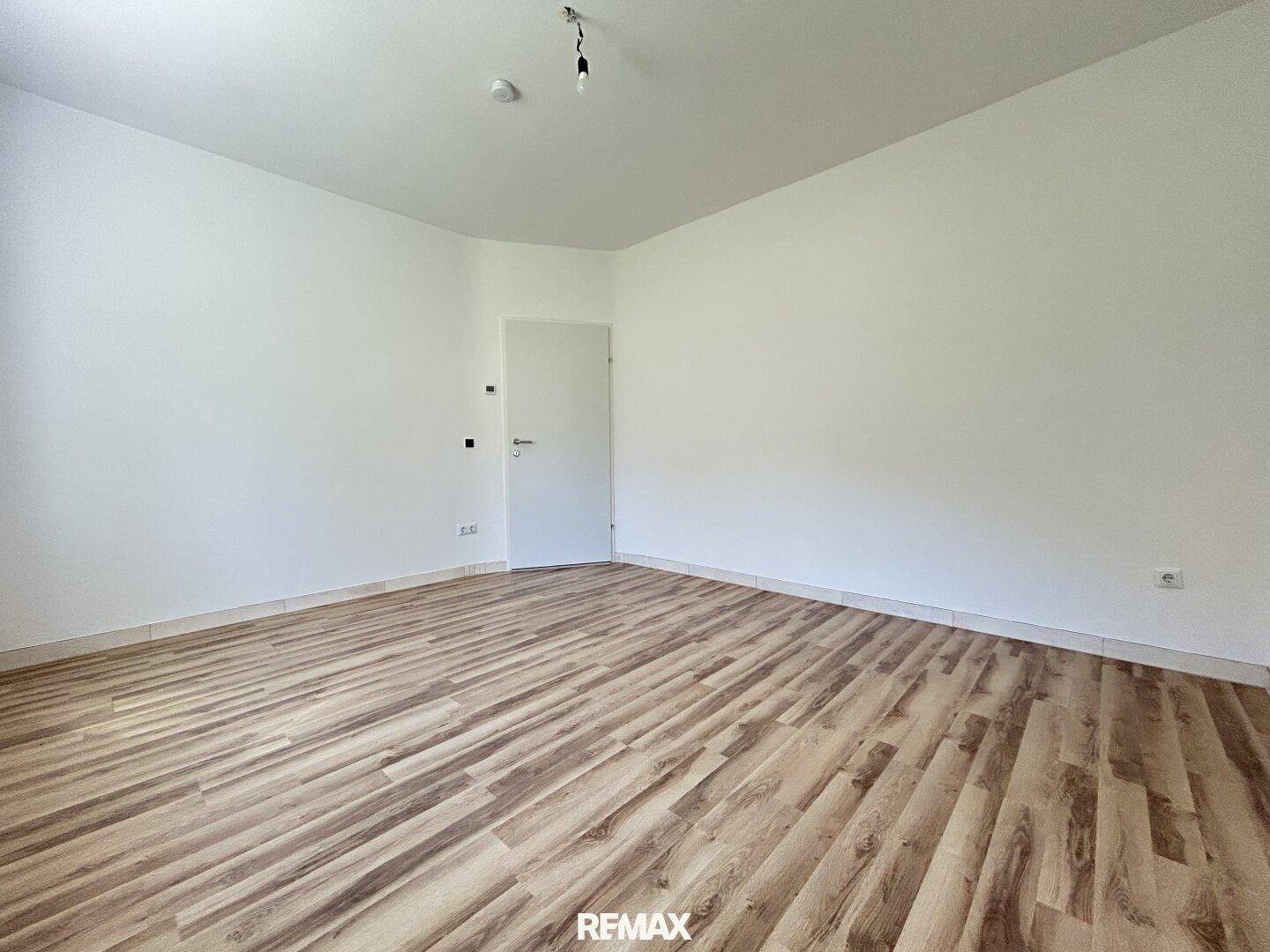 Leeres Schlafzimmer mit Laminatboden und weißen Wänden, bereit zur individuellen Gestaltung.