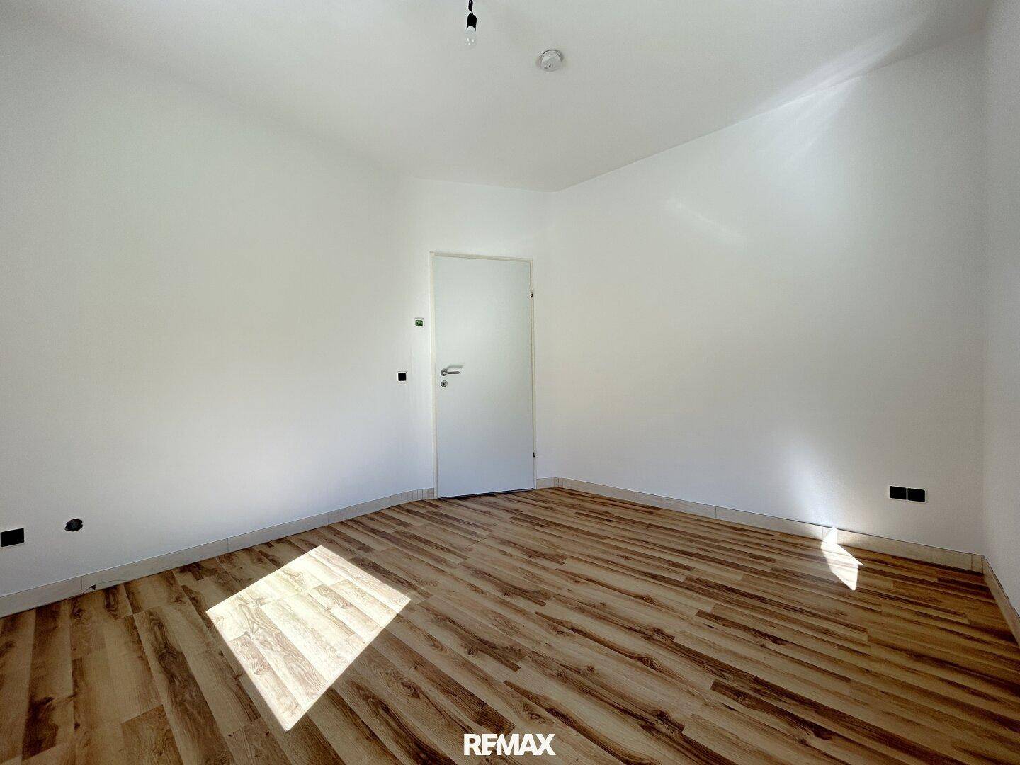 Helles Zimmer mit Laminatboden und weißen Wänden, ideal als Kinder- oder Gästezimmer.
