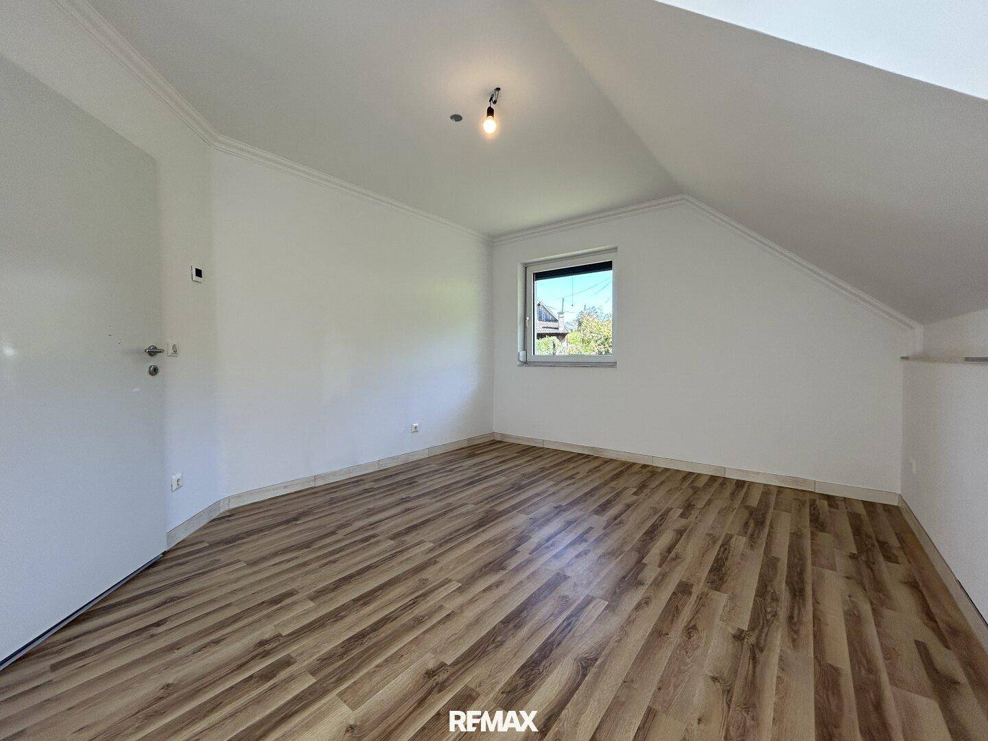 Dachgeschosszimmer mit Laminatboden, Dachschräge und kleinem Fenster.