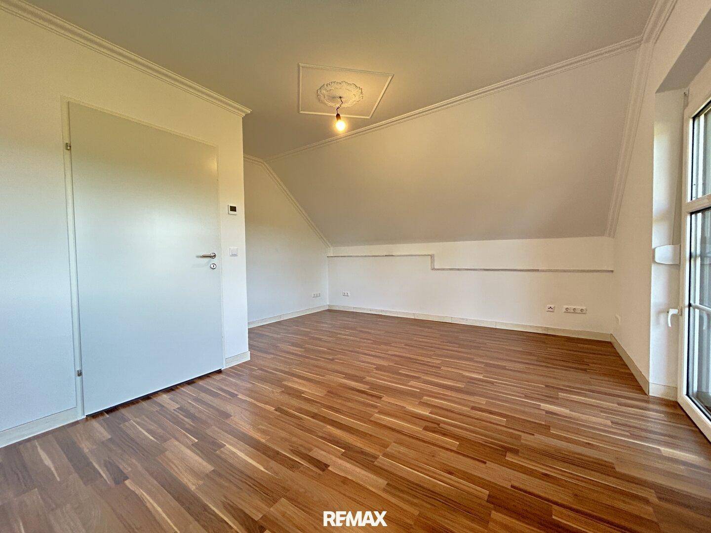 Helles Zimmer im Dachgeschoss mit Holzboden und schrägen Wänden, bereit zur individuellen Gestaltung.