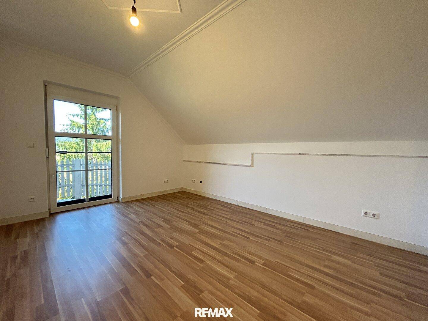Geräumiges Dachgeschosszimmer mit Laminatboden und Zugang zu einem möglichen Balkon.