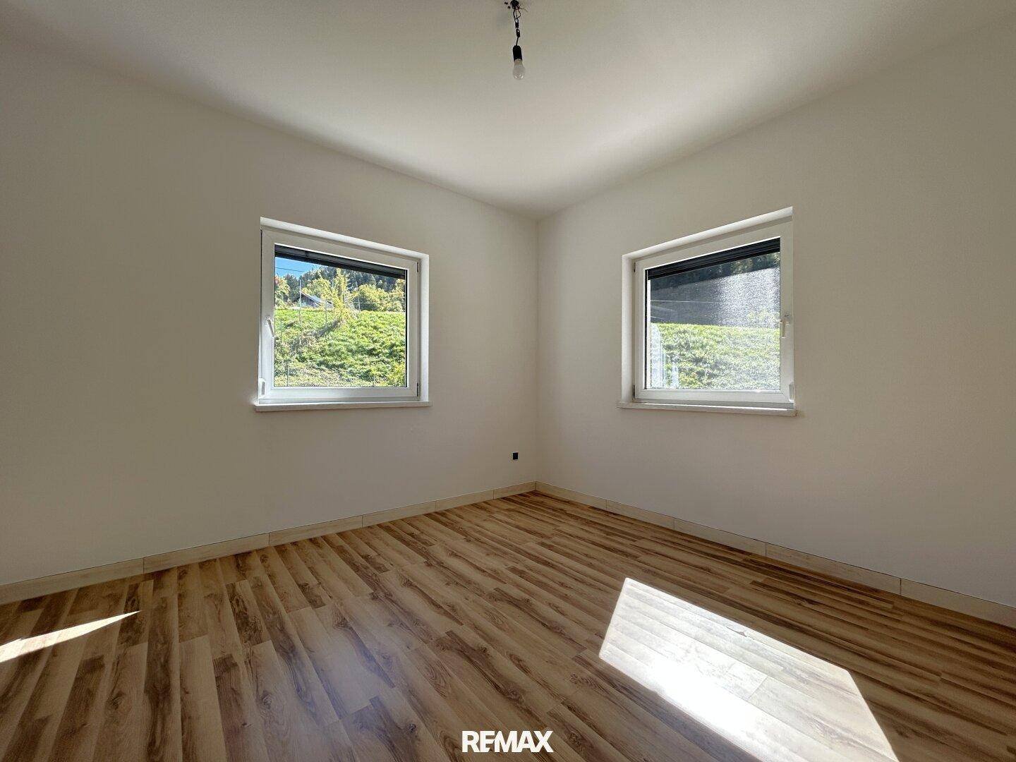 Geräumiges Zimmer mit Laminatboden und zwei Fenstern, die viel Tageslicht hereinlassen.