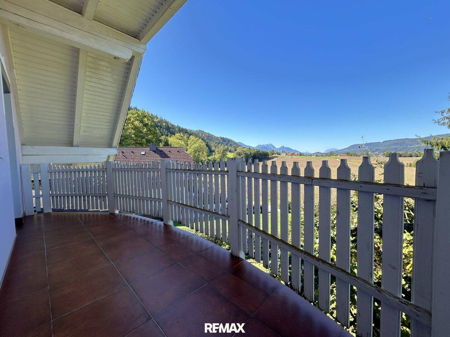 Balkon mit rustikalem Holzzaun und weitem Blick über Felder und die umliegende Berglandschaft.