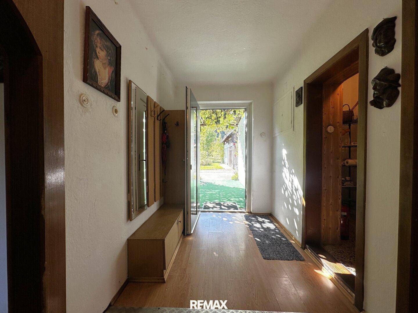 Heller Eingangsbereich mit Holzfußboden, Garderobe und Blick ins Grüne.