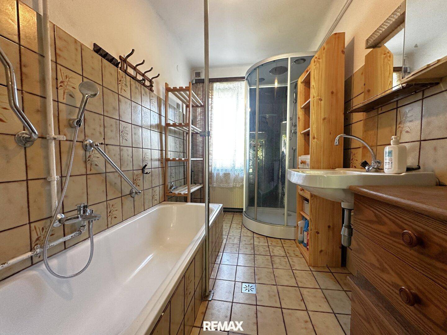 Badezimmer mit Badewanne, Duschkabine und rustikalen Fliesen.