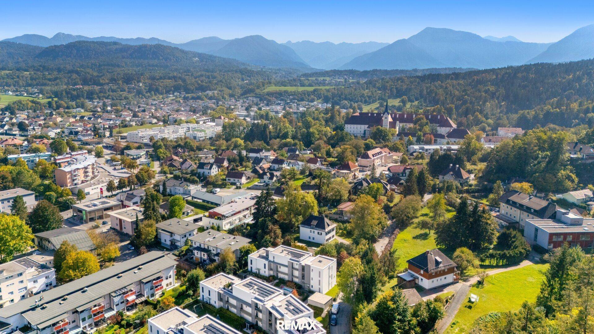 Weitläufige Luftaufnahme eines Wohngebiets mit verschiedenen Gebäuden und Bergpanorama im Hintergrund.