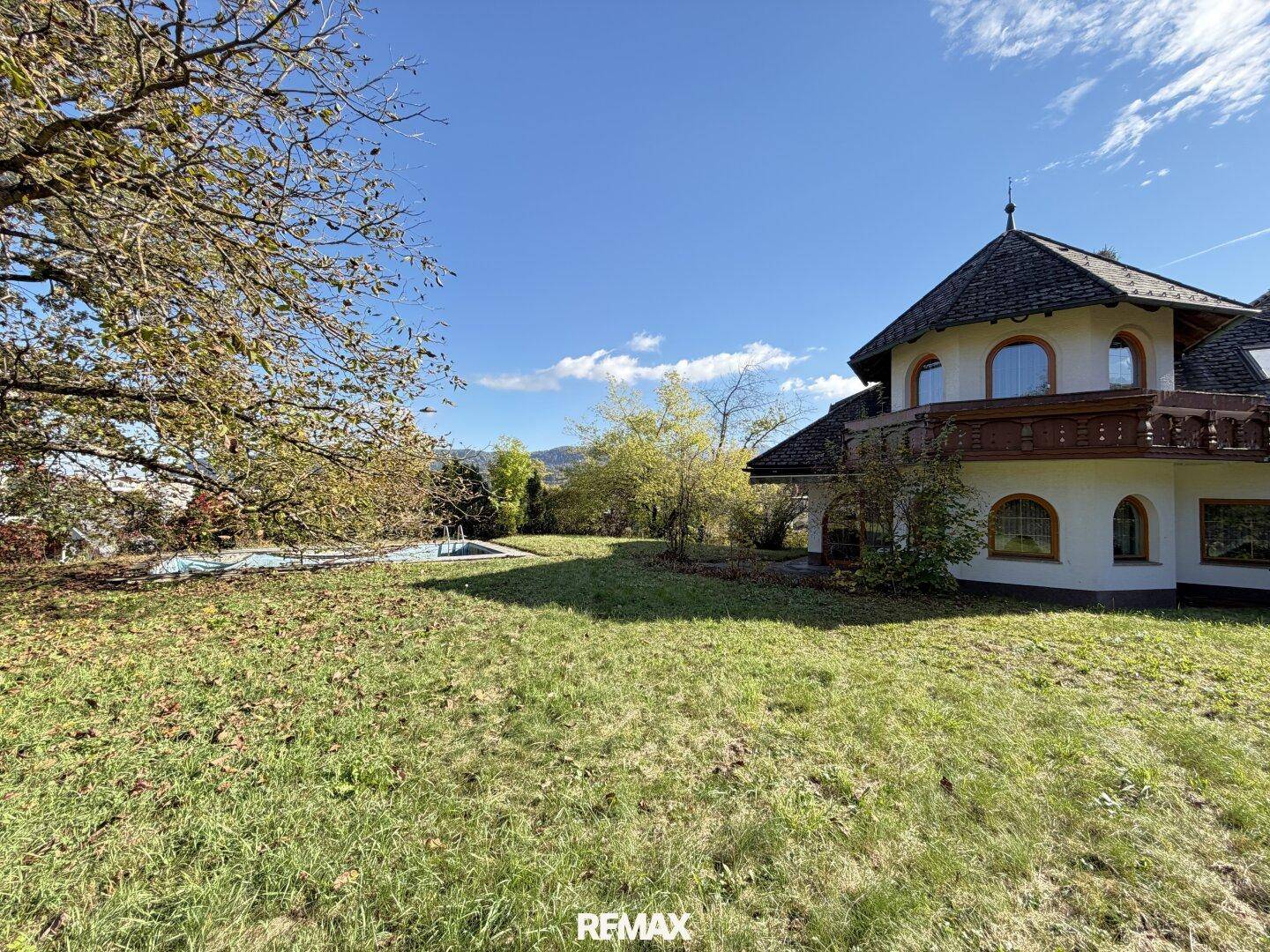 Sonnige Rasenfläche des Gartens mit einem Pool und dem Haus im traditionellen Stil.