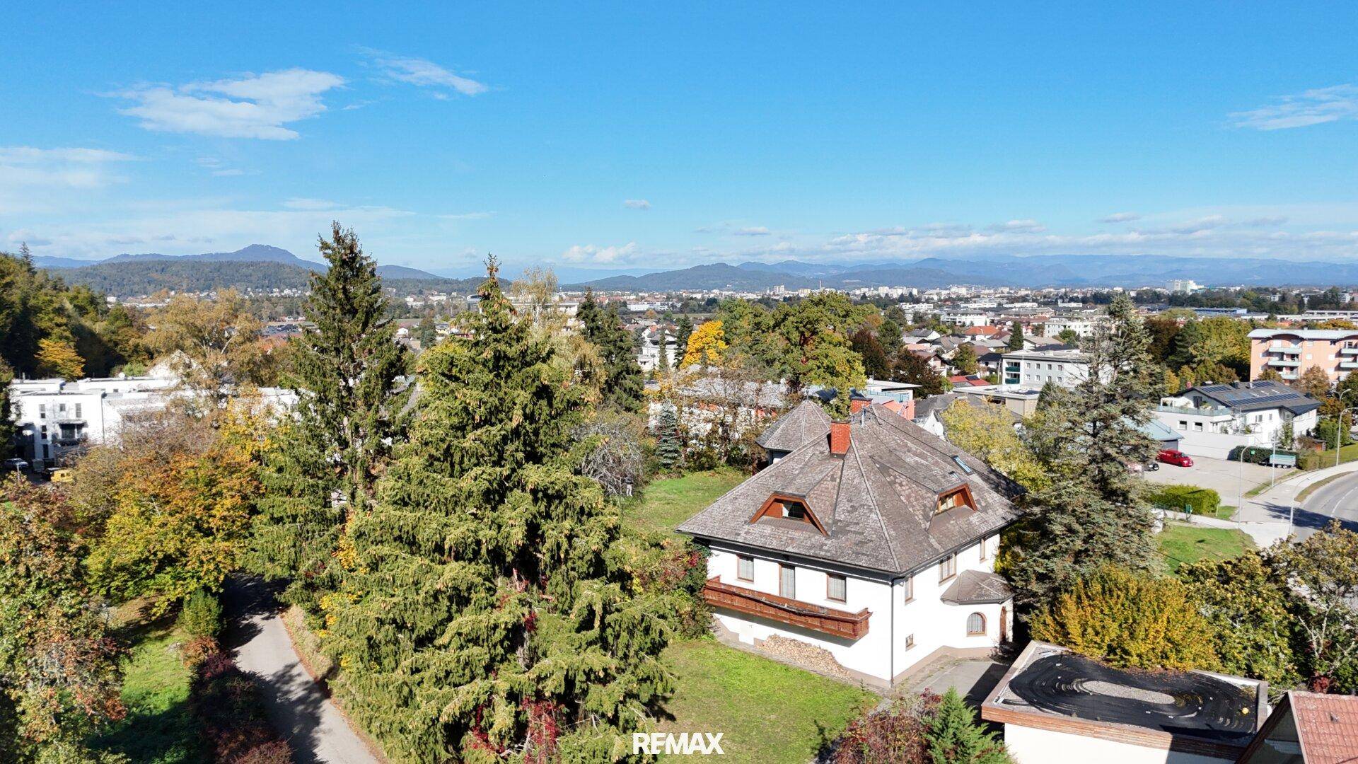 Luftaufnahme eines Hauses mit Satteldach, umgeben von Bäumen und Blick auf die Stadt.