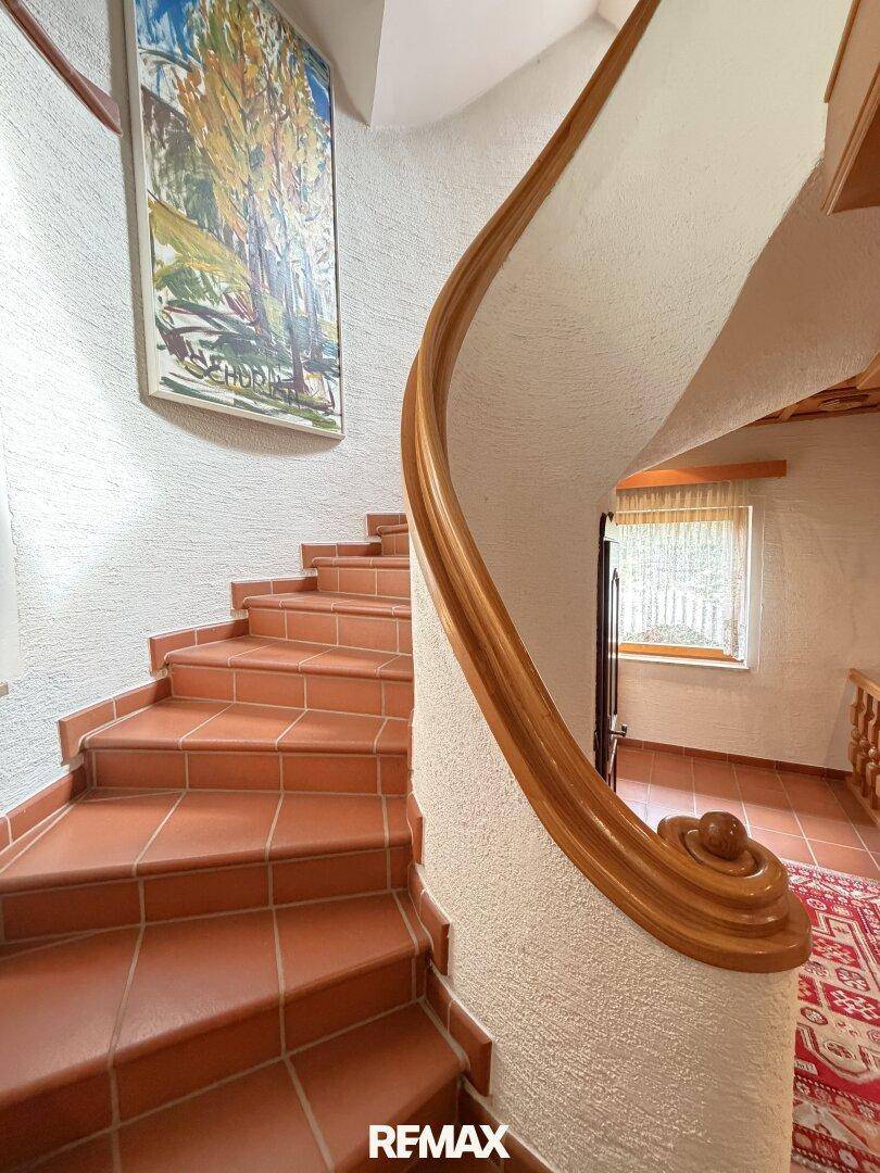 Detailansicht der geschwungenen Holztreppe mit Terrakotta-Stufen und rustikalem Geländer.