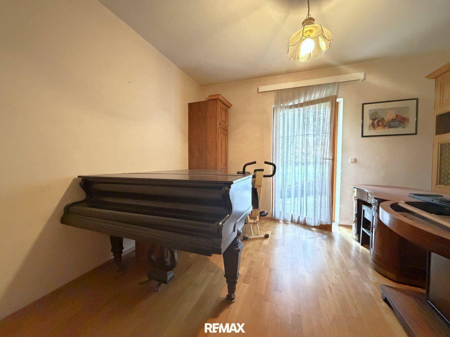 Zimmer mit Holzboden, Klavier und Zugang zu einem Balkon oder einer Terrasse.