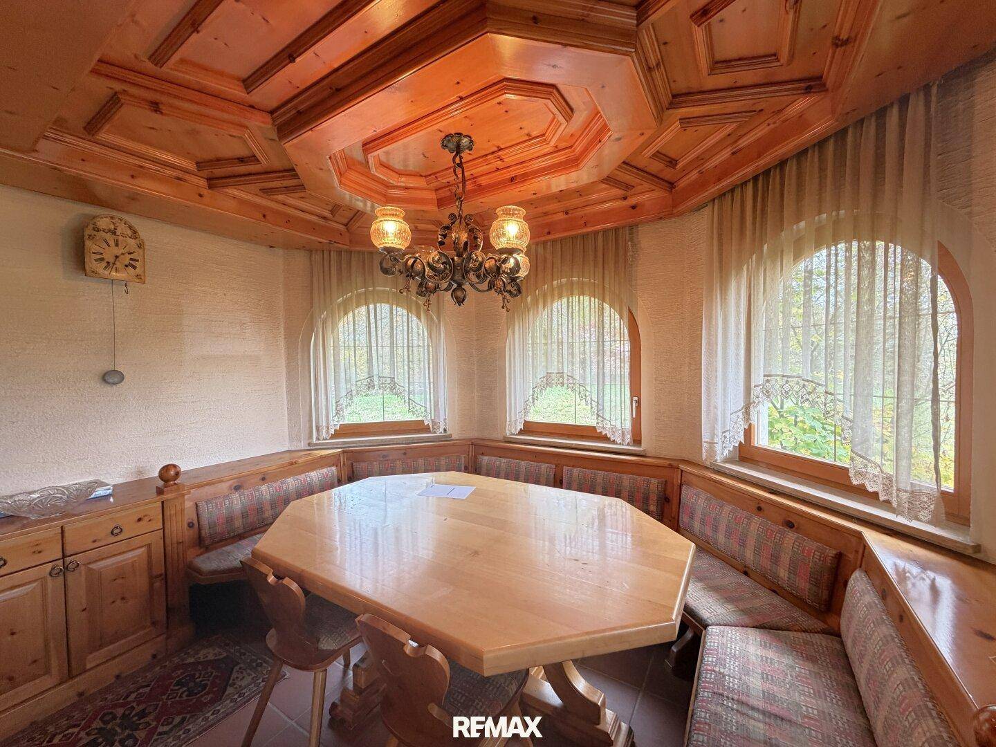 Traditioneller Essbereich mit holzvertäfelter Decke, Eckbank und großen Rundbogenfenstern.