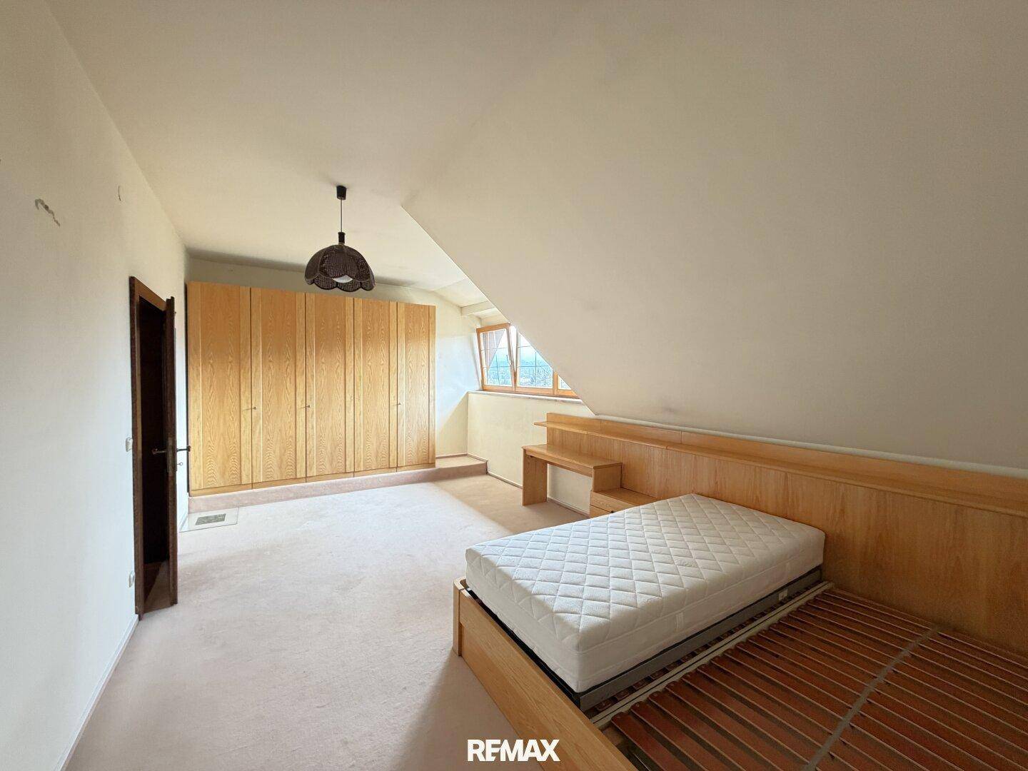 Helles Schlafzimmer im Dachgeschoss mit schräger Decke, Teppichboden und Einbauschränken aus Holz.