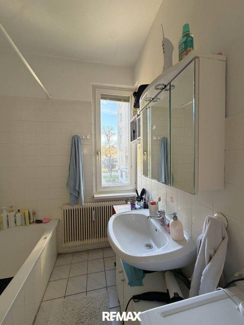 Badezimmer mit Badewanne, Waschbecken, Spiegelschrank und einem Fenster für natürliche Belüftung.
