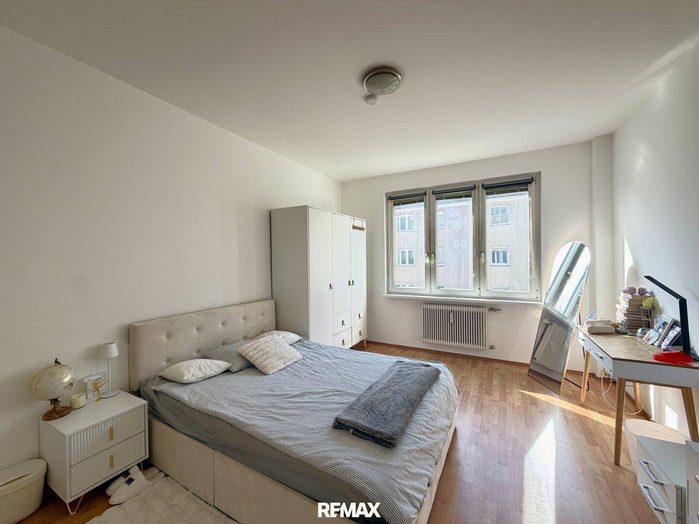Schlafzimmer mit Doppelbett, Holzboden und einem großen Fenster, das viel Tageslicht hereinlässt.