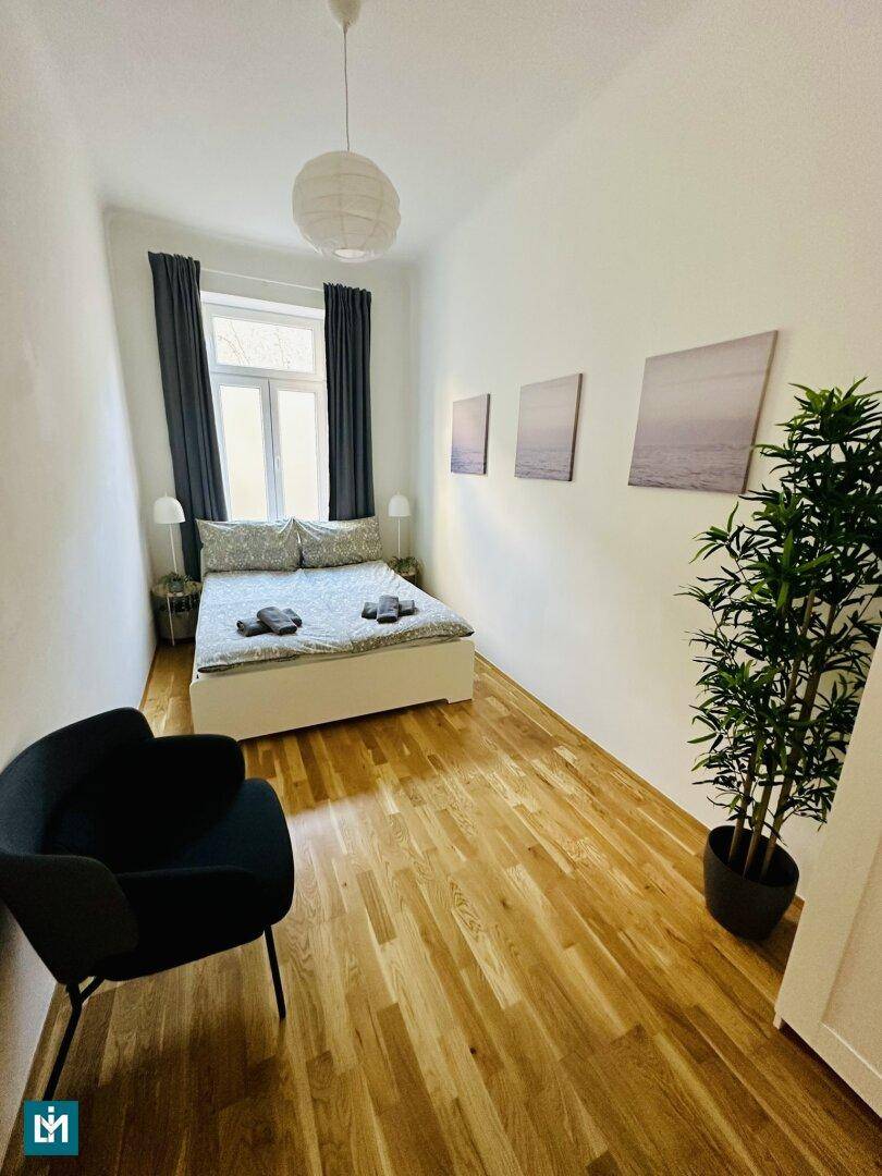 Helles Schlafzimmer mit Parkettboden, Einzelbett und einem großen Fenster für viel Tageslicht.