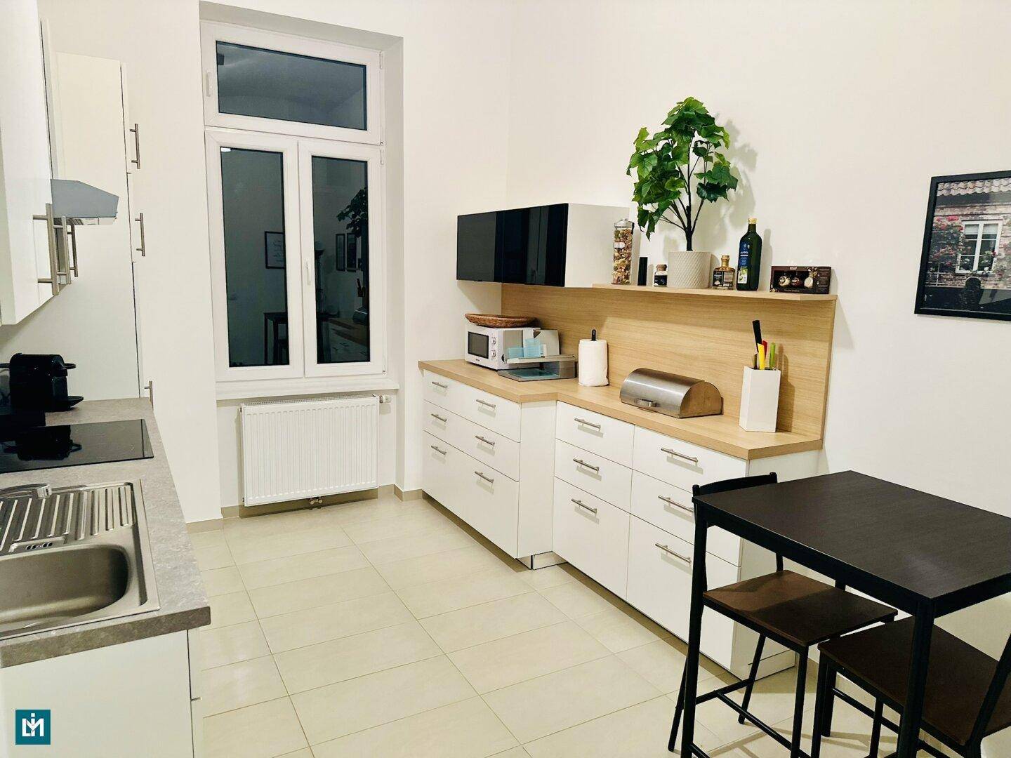 Funktionale Küche mit weißen Schränken, Kochfeld und einem kleinen Essbereich am Fenster.