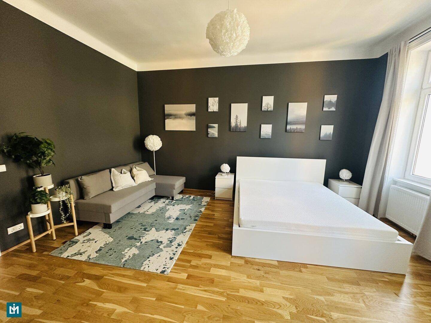 Geräumiges Schlafzimmer mit dunkler Akzentwand, Doppelbett und gemütlicher Sitzecke.