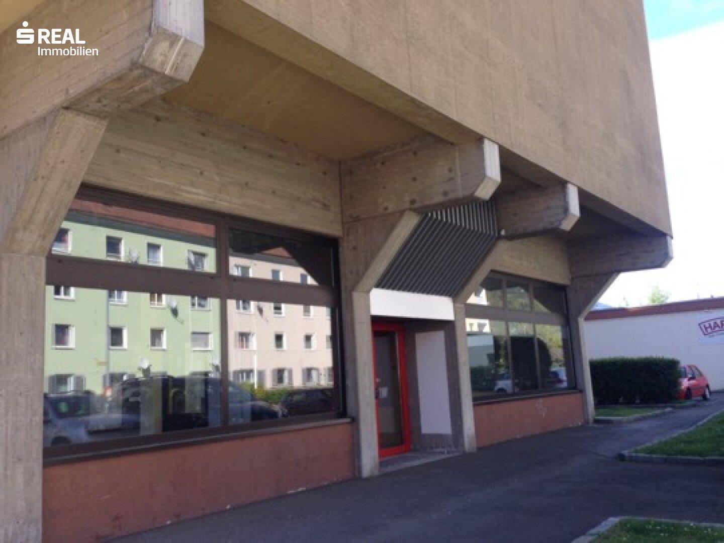 Nahaufnahme der Gebäudefassade im Erdgeschoss mit großen Fenstern und einem Eingangsbereich.