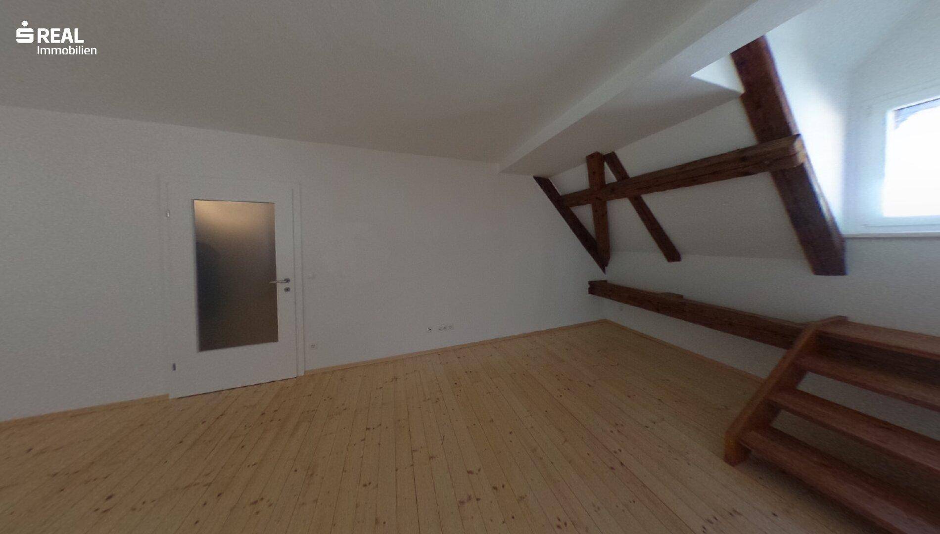 Helles Schlafzimmer im Dachgeschoss mit Holzboden und sichtbaren Holzbalken, bereit zur Einrichtung.
