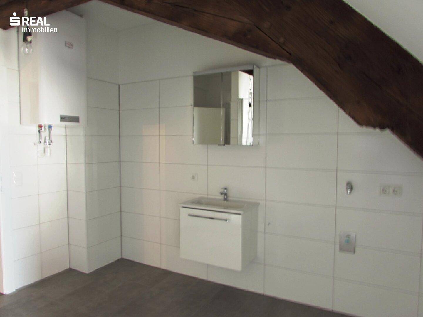 Badezimmer im Dachgeschoss mit weißen Fliesen, Waschbecken und sichtbaren Holzbalken.