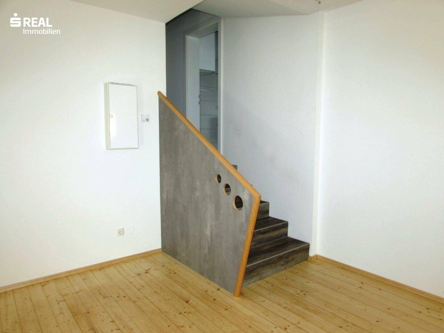 Heller Raum mit Holzboden und einer modernen Treppe, die zu einem oberen Bereich führt.