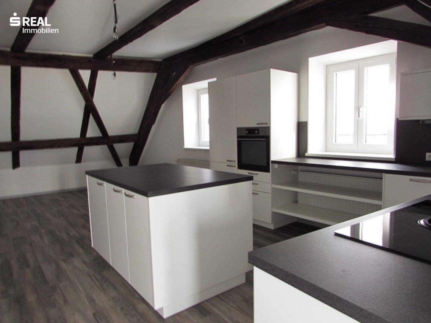 Moderne Küche im Dachgeschoss mit weißen Schränken, dunklen Arbeitsplatten und sichtbaren Holzbalken.