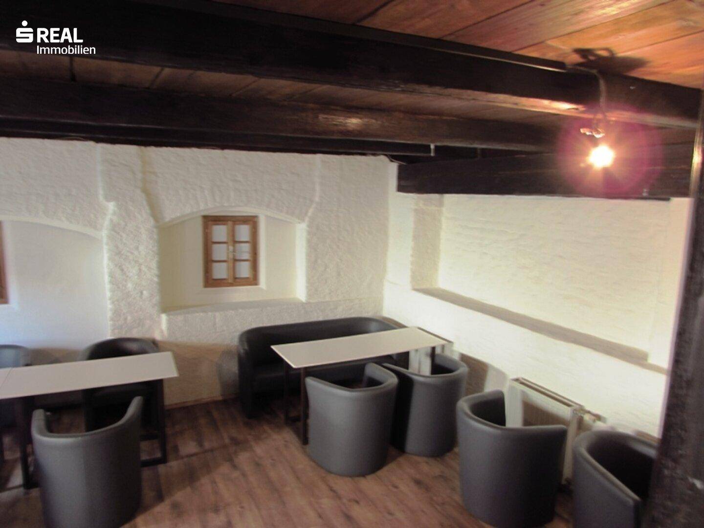 Rustikaler Lounge-Bereich mit Holzbalken, weiß getünchten Wänden und bequemen Sitzgelegenheiten.
