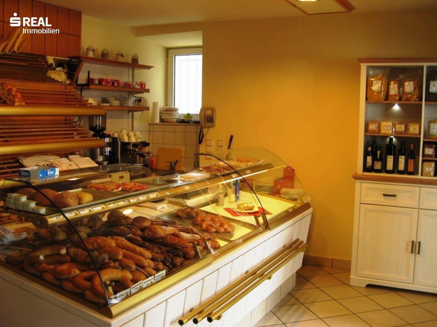 Innenansicht einer Bäckerei mit Auslage voller Backwaren und Regalen mit Produkten.