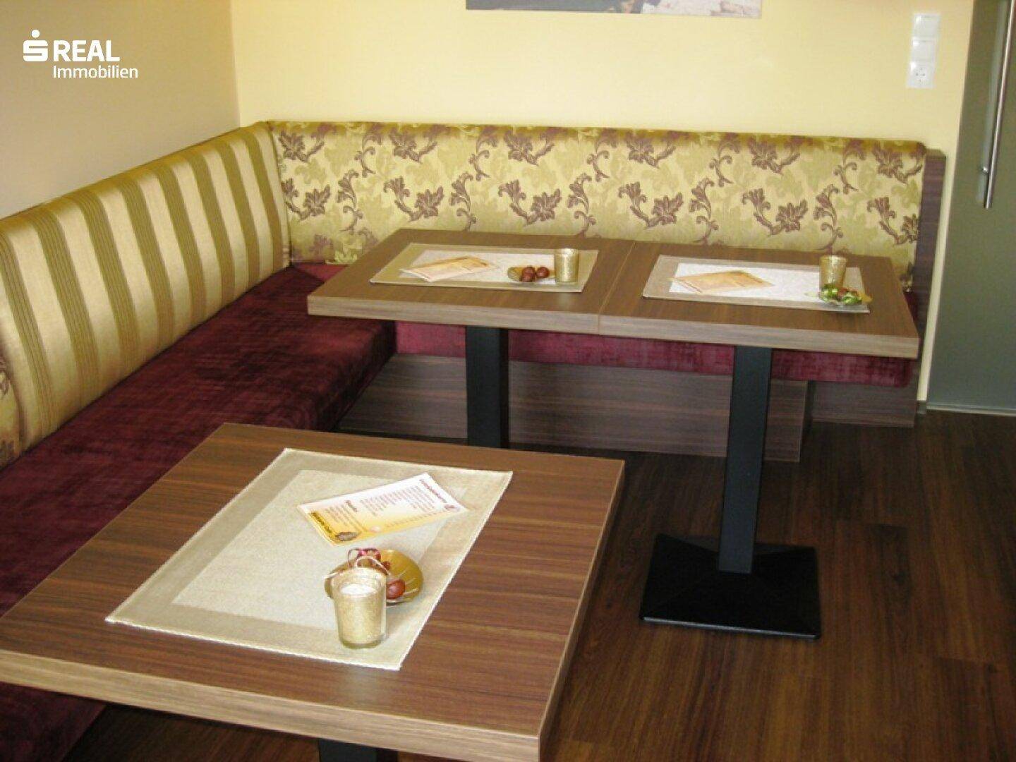 Gemütlicher Sitzbereich mit Eckbank und Holztischen, ideal für ein Café oder Bistro.