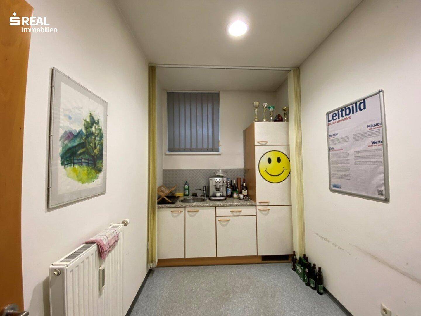 Kleine Küchenzeile mit Spüle, Unterschränken und Kühlschrank in einem Büroraum.