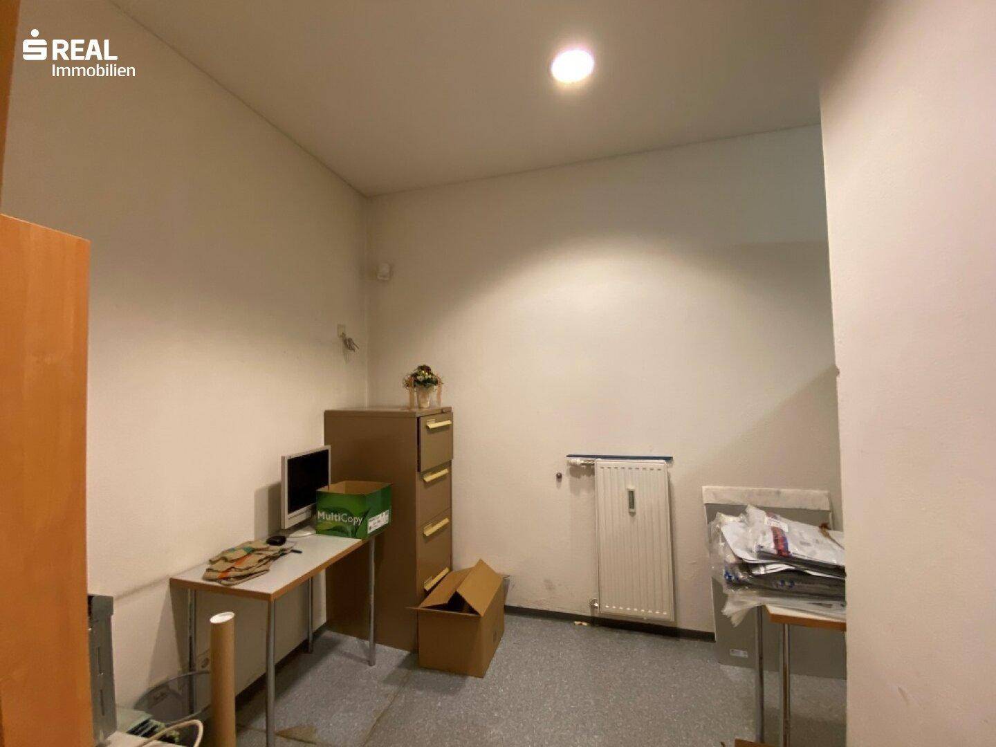 Abstellraum mit Schreibtisch, Regal und Heizkörper, genutzt als Lager- oder Arbeitsbereich.