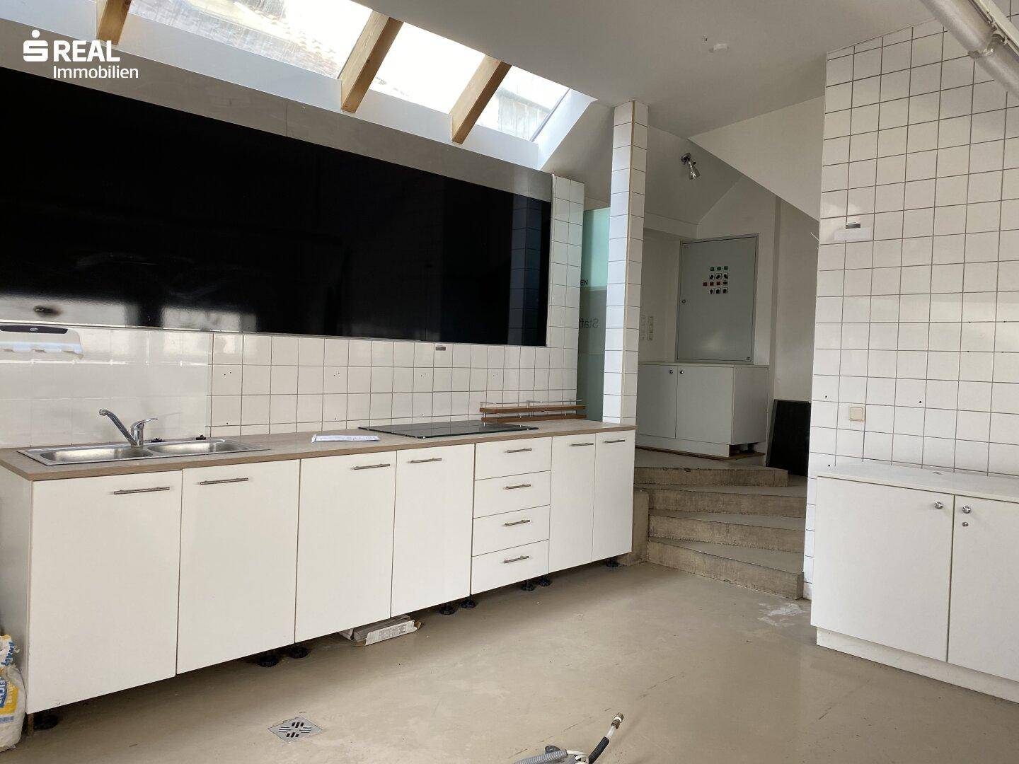 Helle Küche mit weißen Schränken, gefliester Wand und Dachfenstern für eine freundliche Atmosphäre.