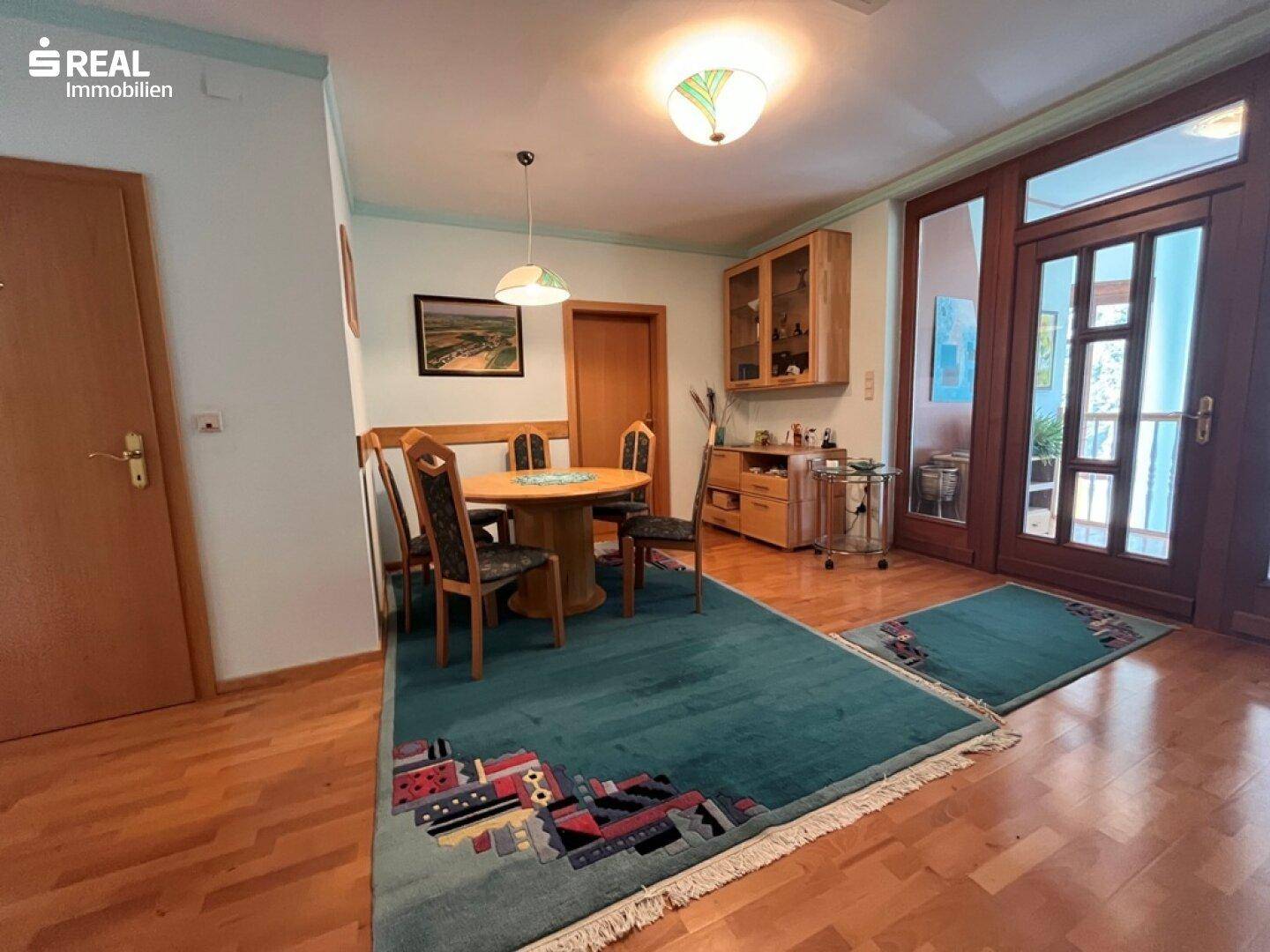 Gemütlicher Essbereich mit Holztisch, Teppich und Zugang zu einem Außenbereich durch große Glastüren.