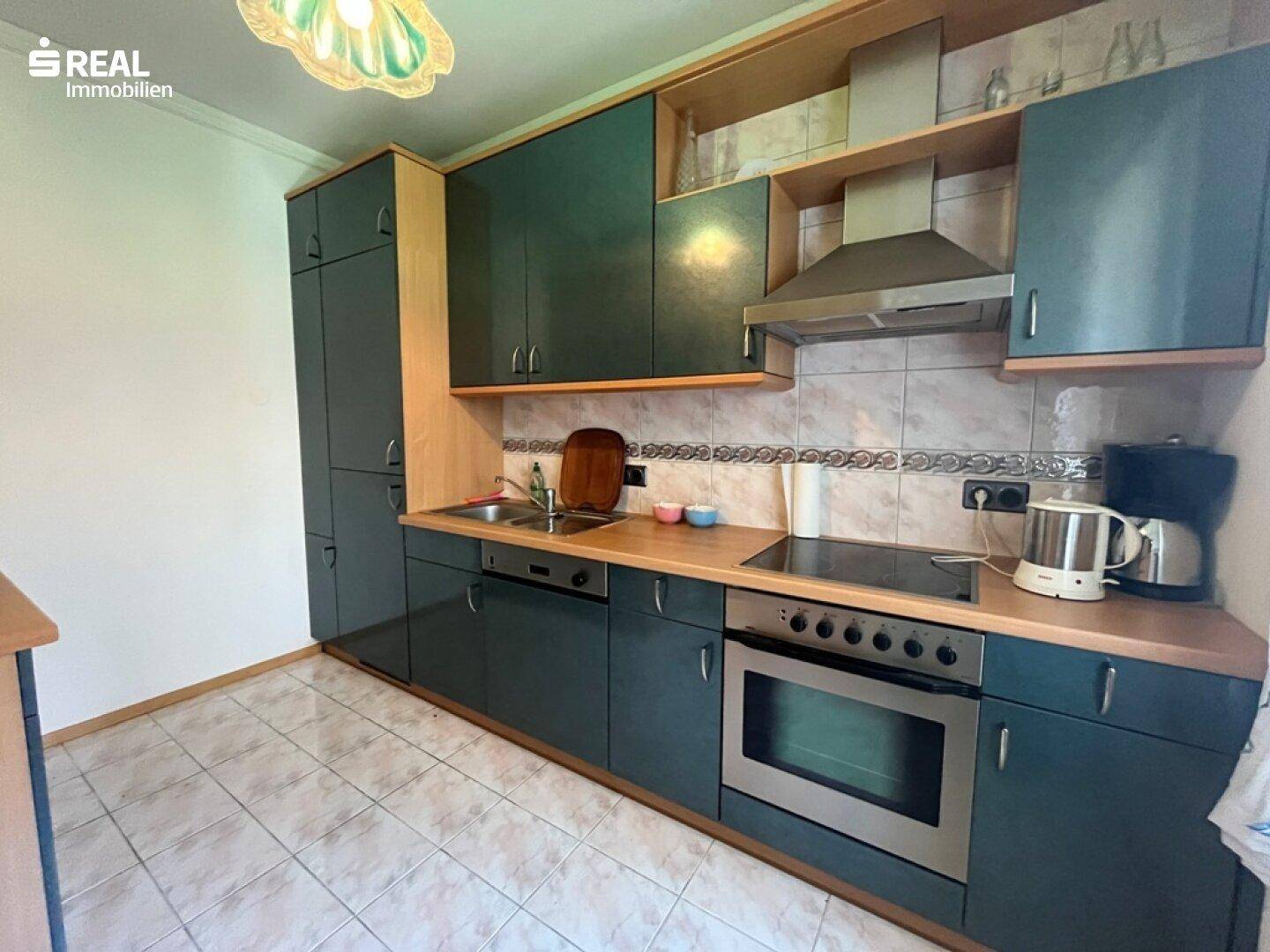 Funktionale Küche mit dunkelgrünen Schränken, Holzarbeitsplatte, Spüle und integriertem Herd mit Backofen.