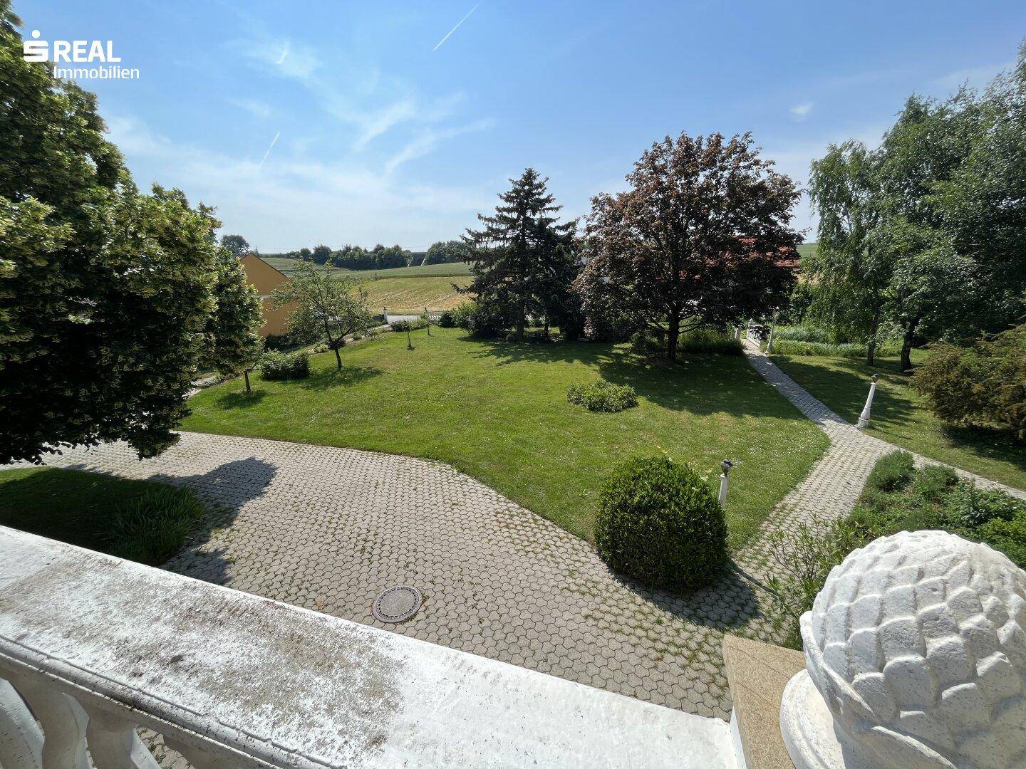 Panoramablick von der Terrasse über den gepflegten Garten und die umliegende grüne Landschaft.