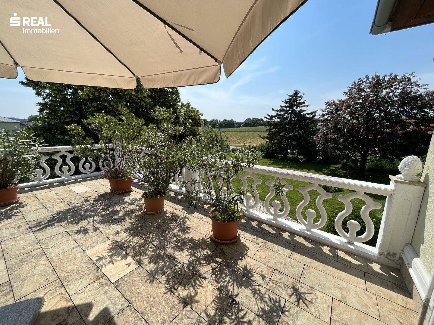 Helle Terrasse mit dekorativem Geländer, Topfpflanzen und weitem Blick über die Landschaft.