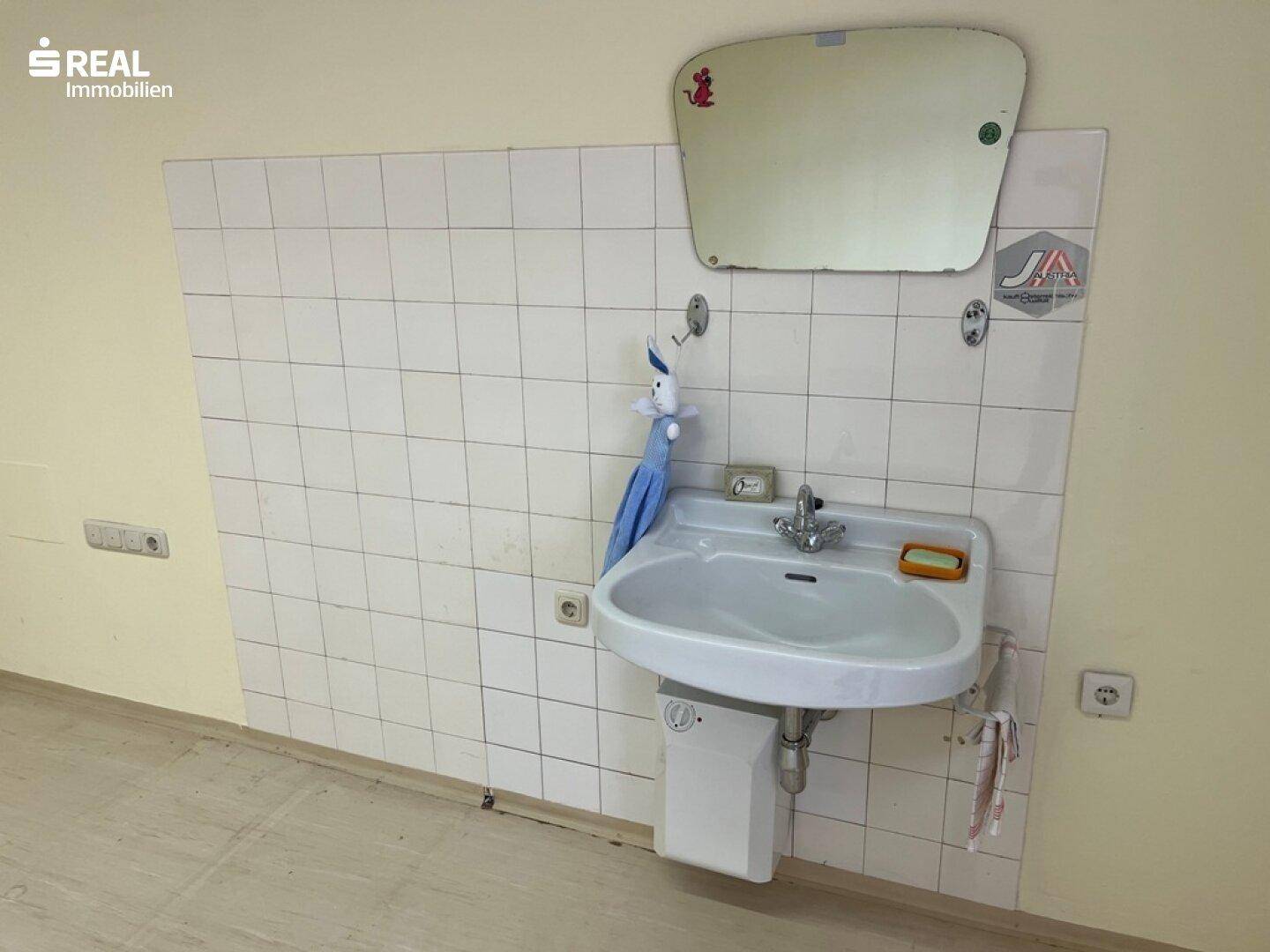 Detailansicht eines Waschbeckens mit Fliesenwand und Spiegel, in einem funktionalen Raum.