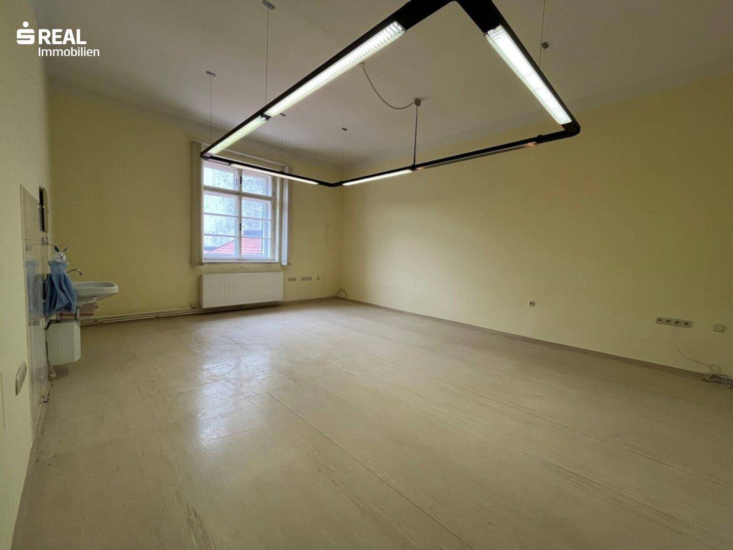 Heller Raum mit einem Waschbecken an der Wand und einem großen Fenster, das Tageslicht spendet.