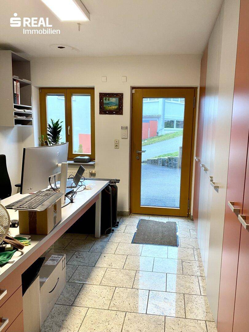 Helles Büro mit Schreibtisch, Computer und einer Tür, die nach draußen führt.