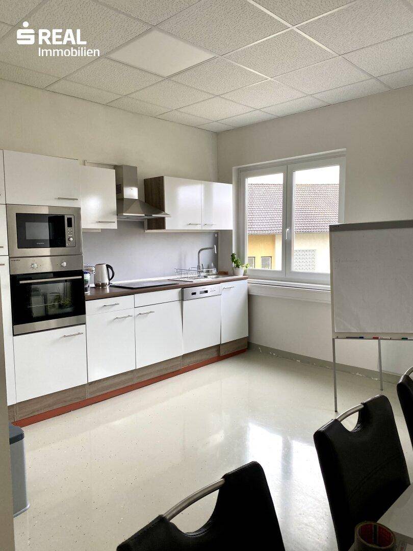 Moderne Küche mit weißen Schränken, Edelstahlgeräten und einem Fenster mit Blick nach draußen.