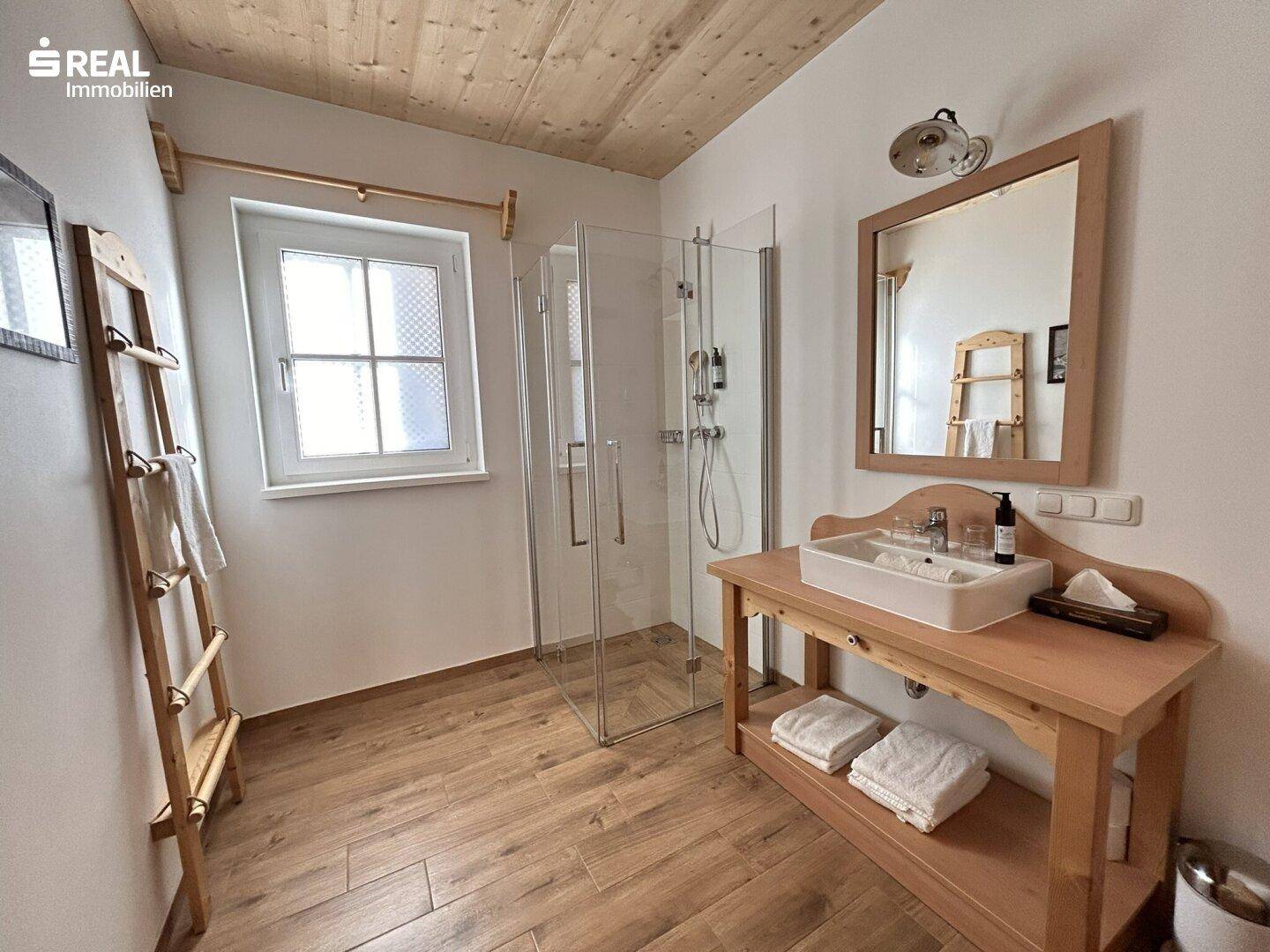 Modernes Badezimmer mit Holzboden, Glasdusche und Holzwaschtisch mit Fenster.