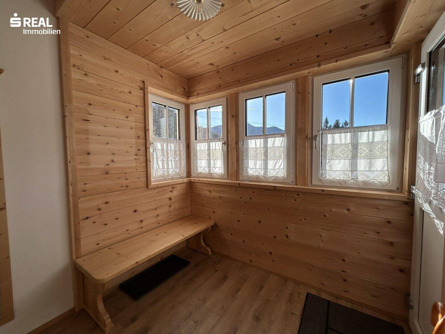 Gemütlicher Eingangsbereich mit Holzvertäfelung, Sitzbank und Fenstern mit Bergblick.