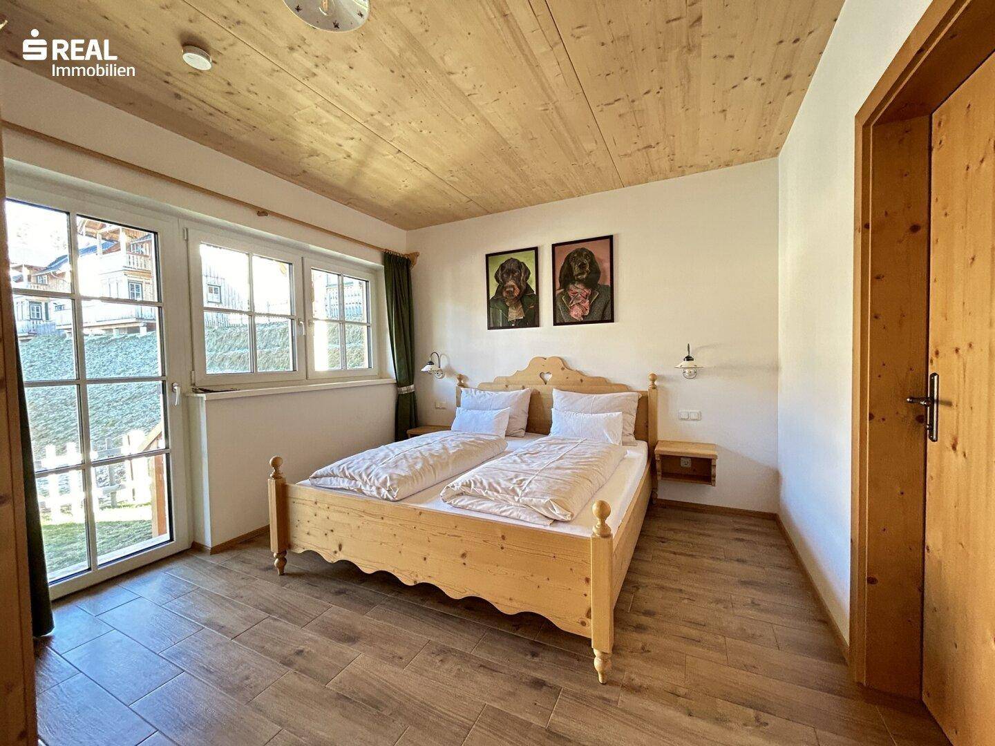 Helles Schlafzimmer mit Holzbett, Holzbalkendecke und Zugang zu einem Balkon mit Ausblick.