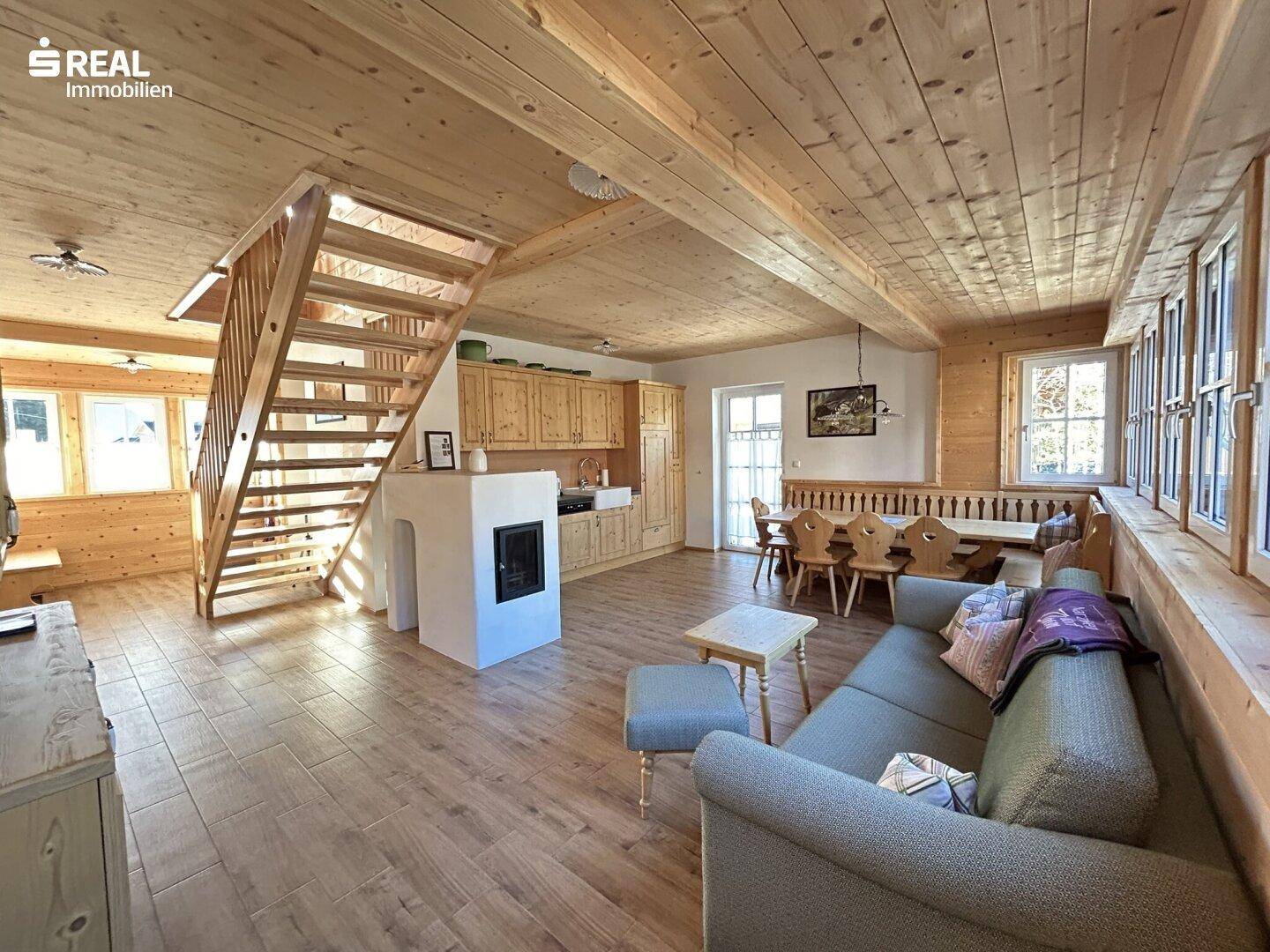 Offener Wohn-Essbereich mit Holzbalkendecke, Kamin und integrierter Küche im Landhausstil.