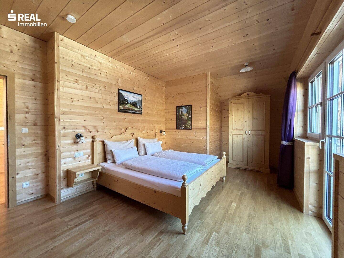 Geräumiges Schlafzimmer mit Holzvertäfelung, Holzbett und Kleiderschrank im Landhausstil.