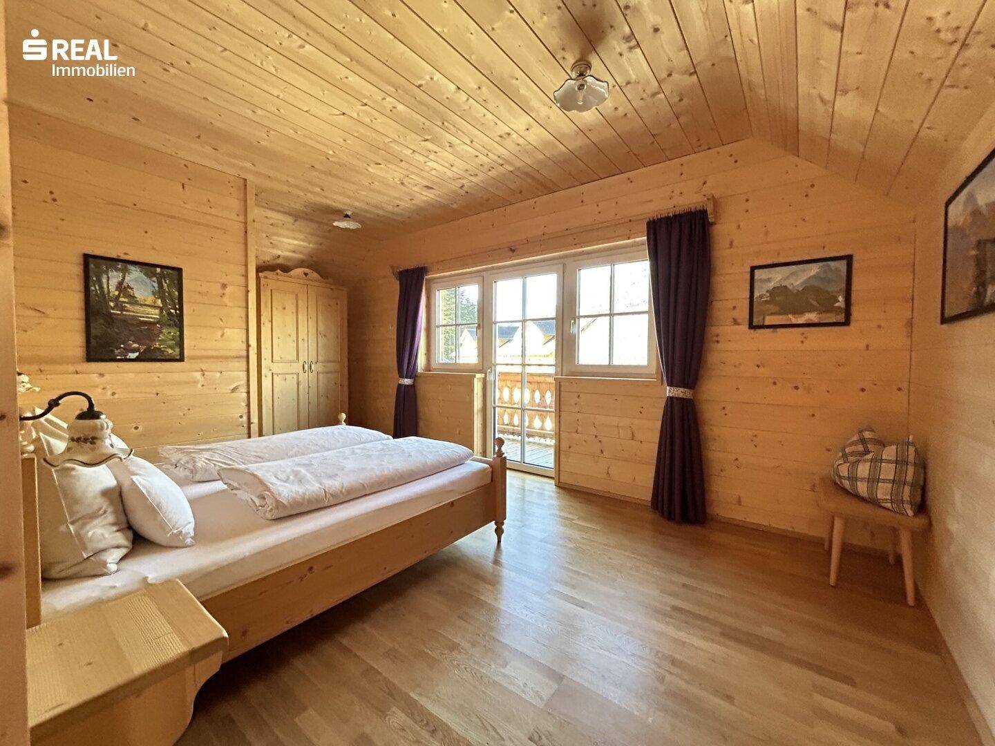 Helles Schlafzimmer mit Holzboden, Holzbalkendecke und Zugang zu einem Balkon mit Ausblick.