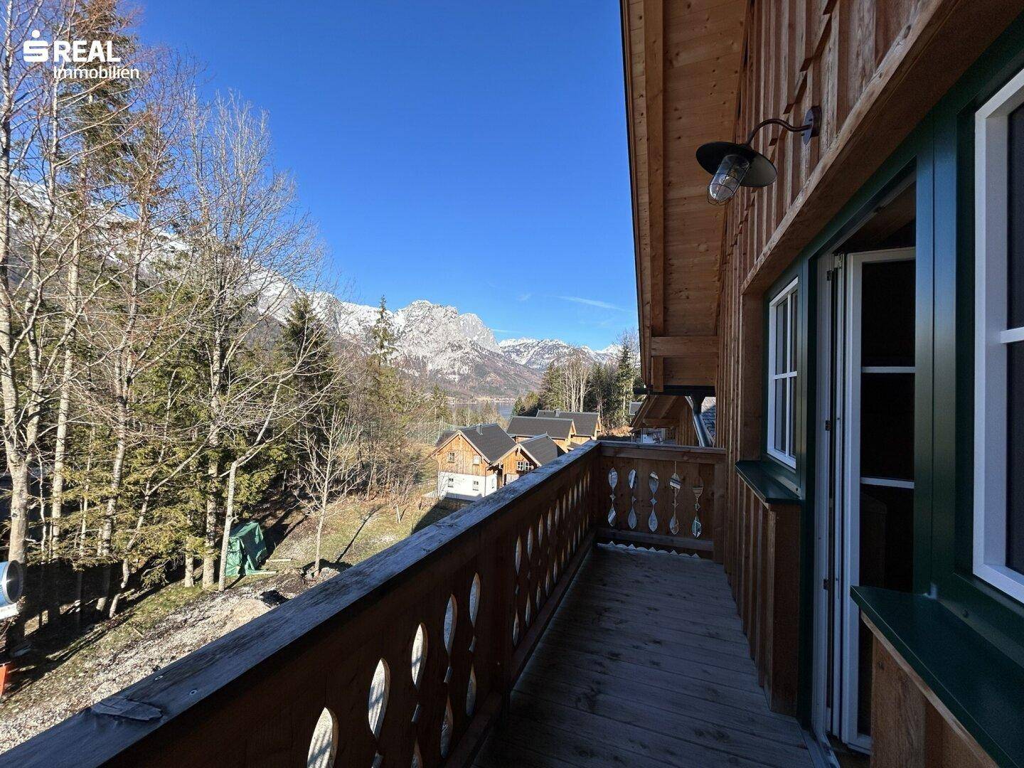 Geräumiger Balkon mit Holzgeländer und weitem Blick auf den See und die umliegende Berglandschaft.